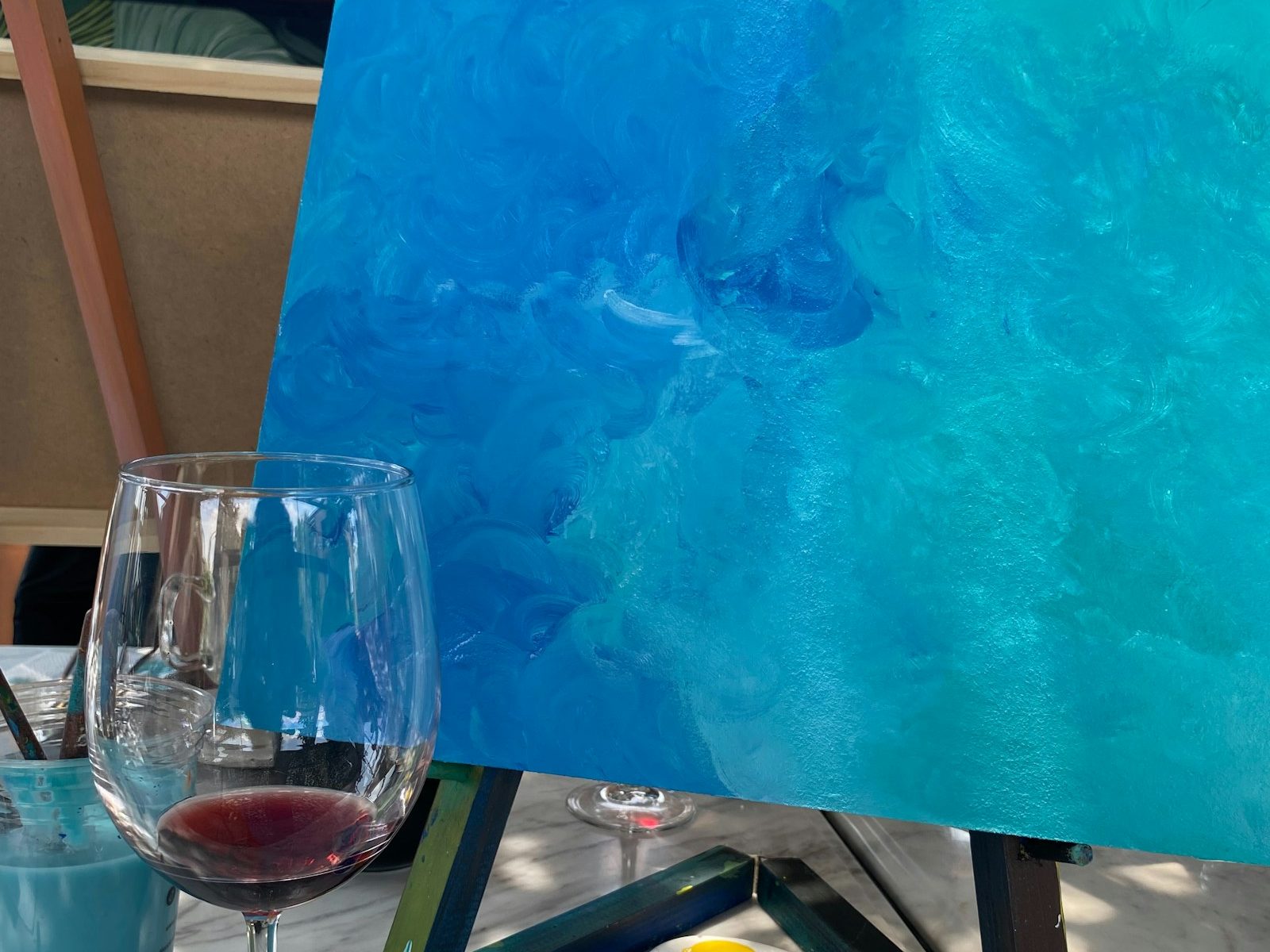 Frische blaue Leinwand auf der Staffelei neben einem Glas Wein
